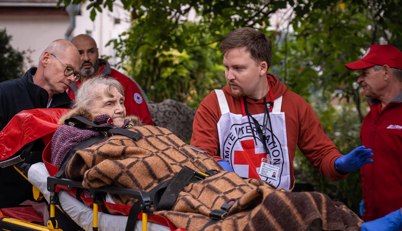 An ICRC medical staff member assists an elderly woman on a stretcher during an emergency situation.