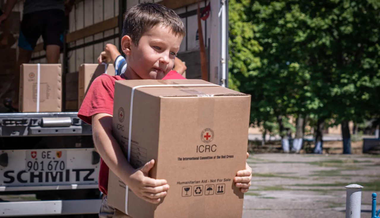 A boy carries a box of assistance items away from the semi-truck.