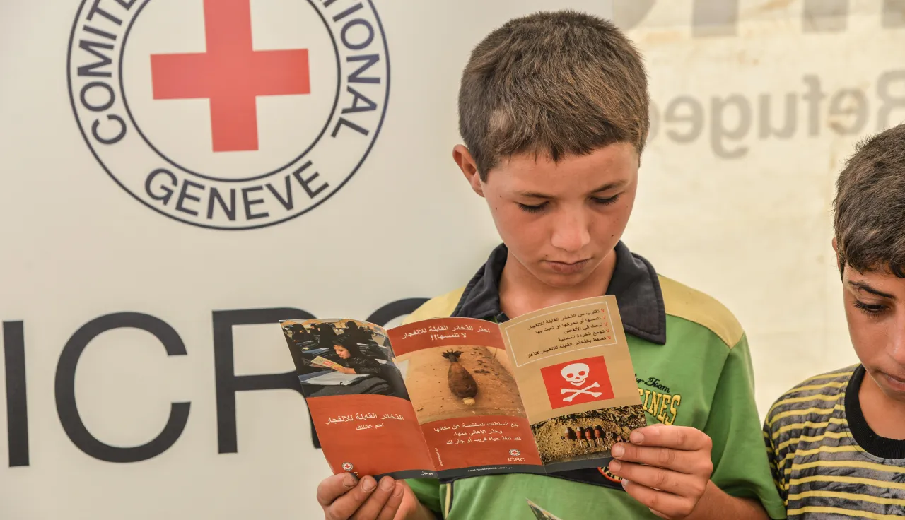 Children read brochures in an awareness session conducted by the ICRC on explosive remnants of war for displaced people.