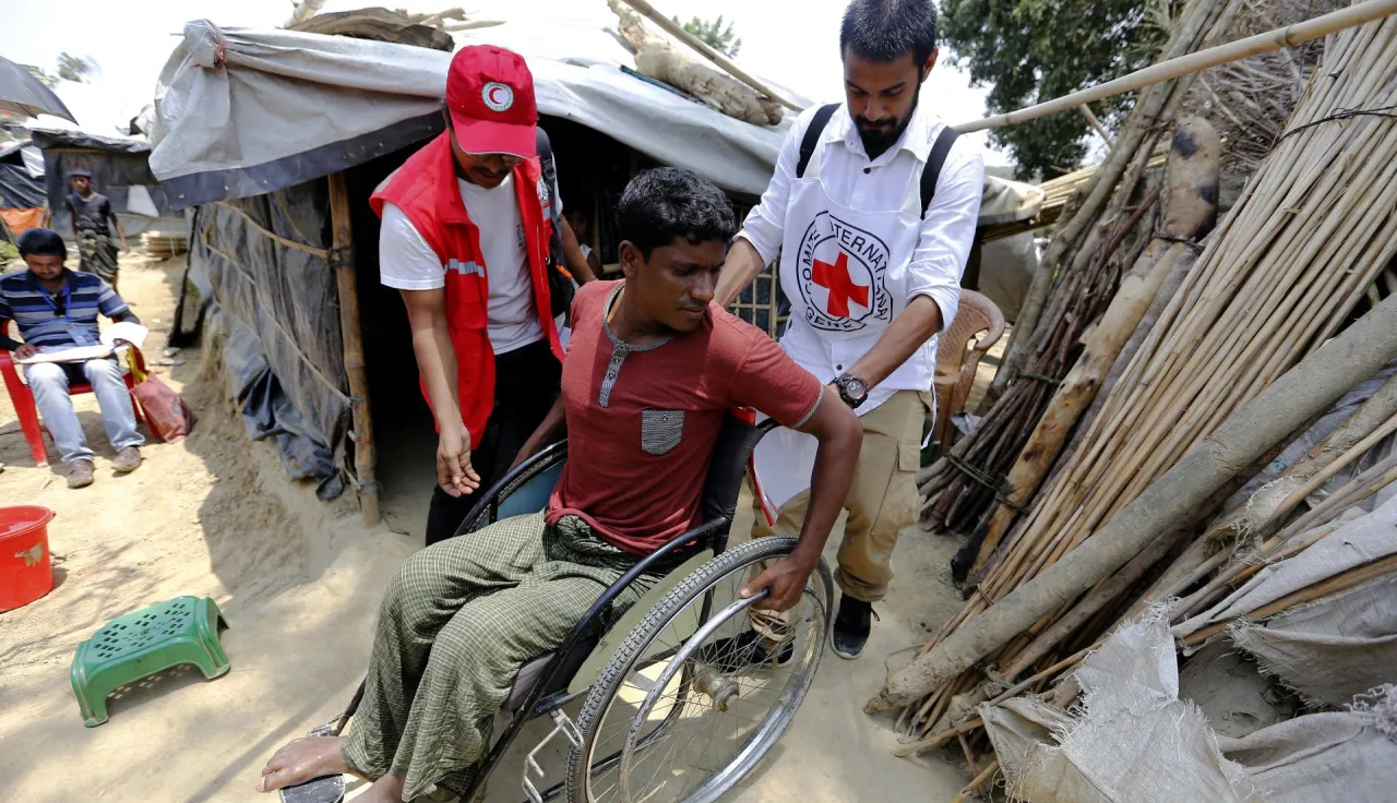 An ICRC field officer and a Bangladesh Red Crescent Society member are assisting a refugee from Myanmar with physical disabilities.