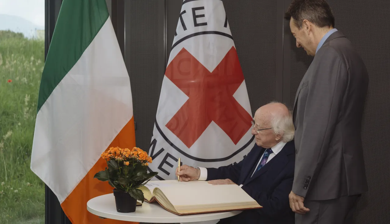 President of Ireland signing visitors' book at ICRC headquarters with the ICRC and Irish flags in the background