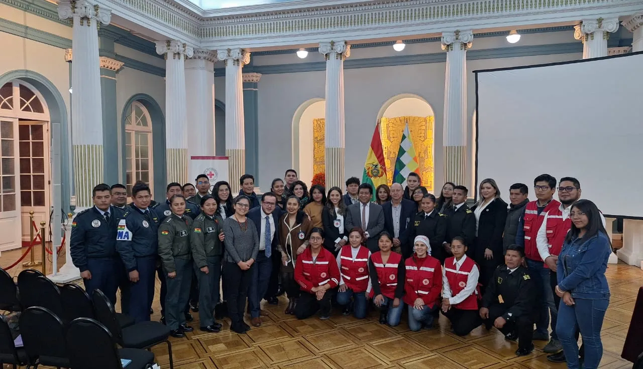 Policías, militares y otros funcionarios con miembros del Movimiento de la Cruz Roja posan para una foto grupal en un salón.