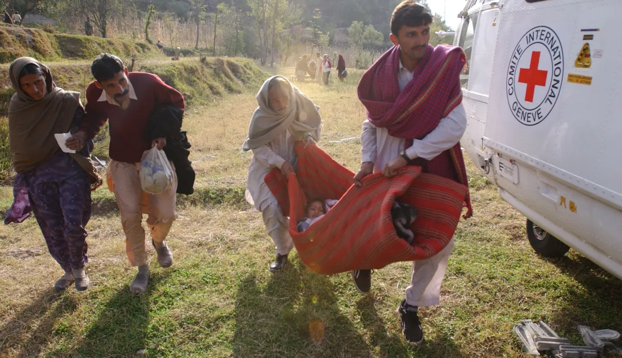 Dos personas trasladan a un paciente envuelto en una manta a un helicóptero del CICR para realizar una evacuación médica de Saidpur a Muzaffarabad, en Pakistán. Fred CLARKE/CICR  Dos personas trasladan a un paciente envuelto en una manta a un helicóptero del CICR para realizar una evacuación médica de Saidpur a Muzaffarabad, en Pakistán.