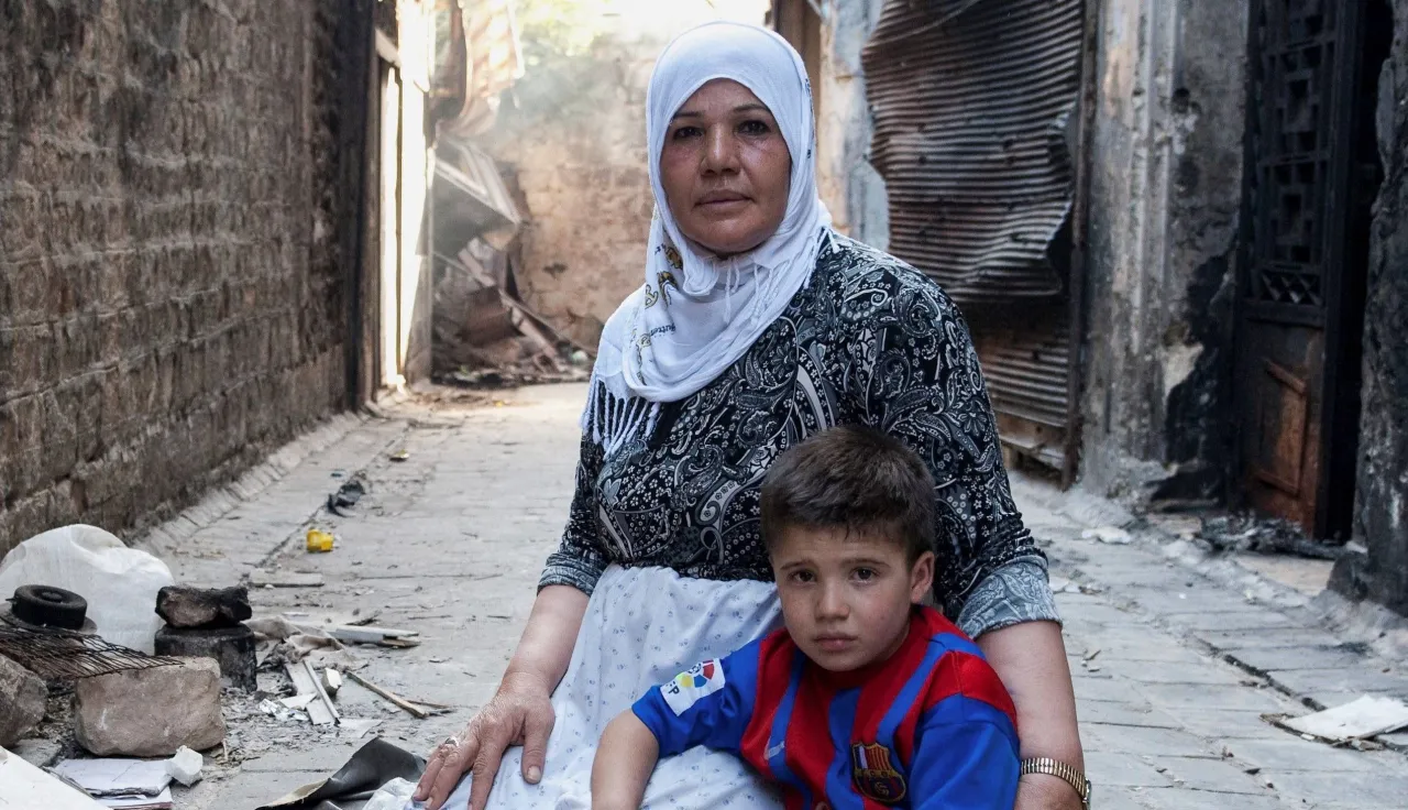 Syria, Aleppo, Jdaideh district. A displaced mother tends to her child and bakes bread in her street alley- merely a block away from the frontline.