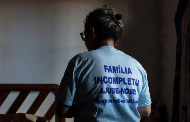 Una mujer de espaldas con una camiseta que dice "Familia incompleta, ayúdenos".