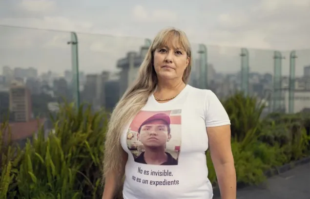Una mujer con una camiseta que muestra a un ser querido desaparecido y la leyenda "No es invisible, no es un expediente"