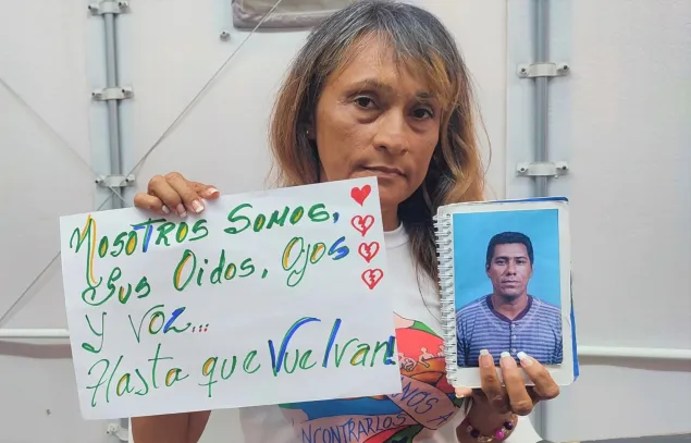 Una mujer sostiene una foto de un ser querido desaparecido y un cartel que dice "nosotros somos sus oídos, sus ojos, su voz... hasta que vuelvan".