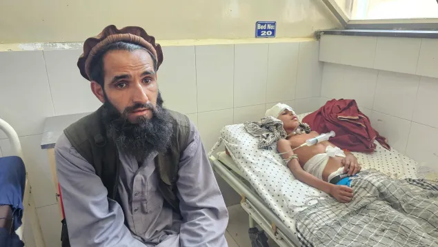 Photo--8-Mohammad-Rahim Afghanistan A man sits on a chair beside a hospital bed where a young boy, with bandages on his head and medical tubes attached, lies injured and resting under a blanket.