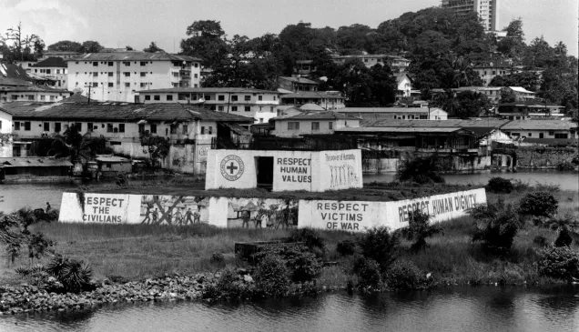 Cidade com paredes pintadas com uma cruz vermelha e textos que dizem "Respete os civis", "Respeite os valores humanos", "Respeite as vítimas da guerra" e "Respeite a dignidade humana".