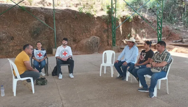 Seis personas, entre ellas dos con el emblema del CICR, sentadas en sillas en un espacio abierto.