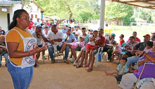 Una persona del CICR se dirige a una comunidad. De fondo se ven varias personas sentadas y prestando atención a la charla.