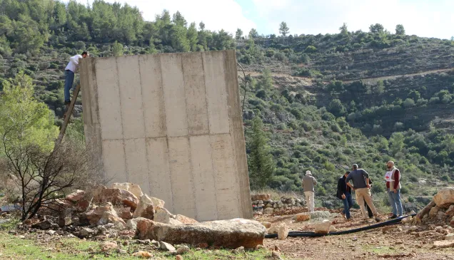 Un hombre subido en una escalera se asoma a una gran estructura de concreto. Abajo hay otros hombres discutiendo. 