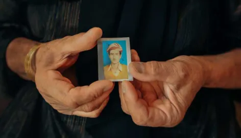 A woman in iraq holds a passport sized photograph of a missing relative