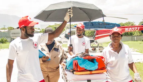 Ambulance workers shield a patient on a stretcher from the sun with an umbrella