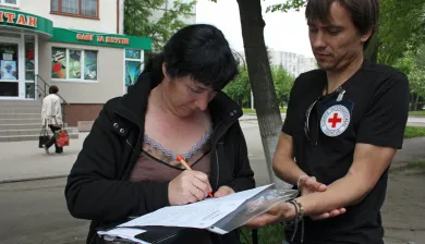 A woman in Ukraine writes a reply to her sister, leaning on Arkadiy's folder, an ICRC employee (2015). Jessica Barry/ICRC