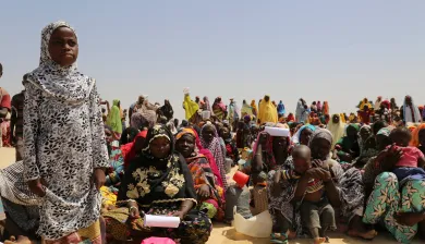 A group of people at an ICRC distribution in Niger. Most seated in the sand, one girl is standing in the foreground.
