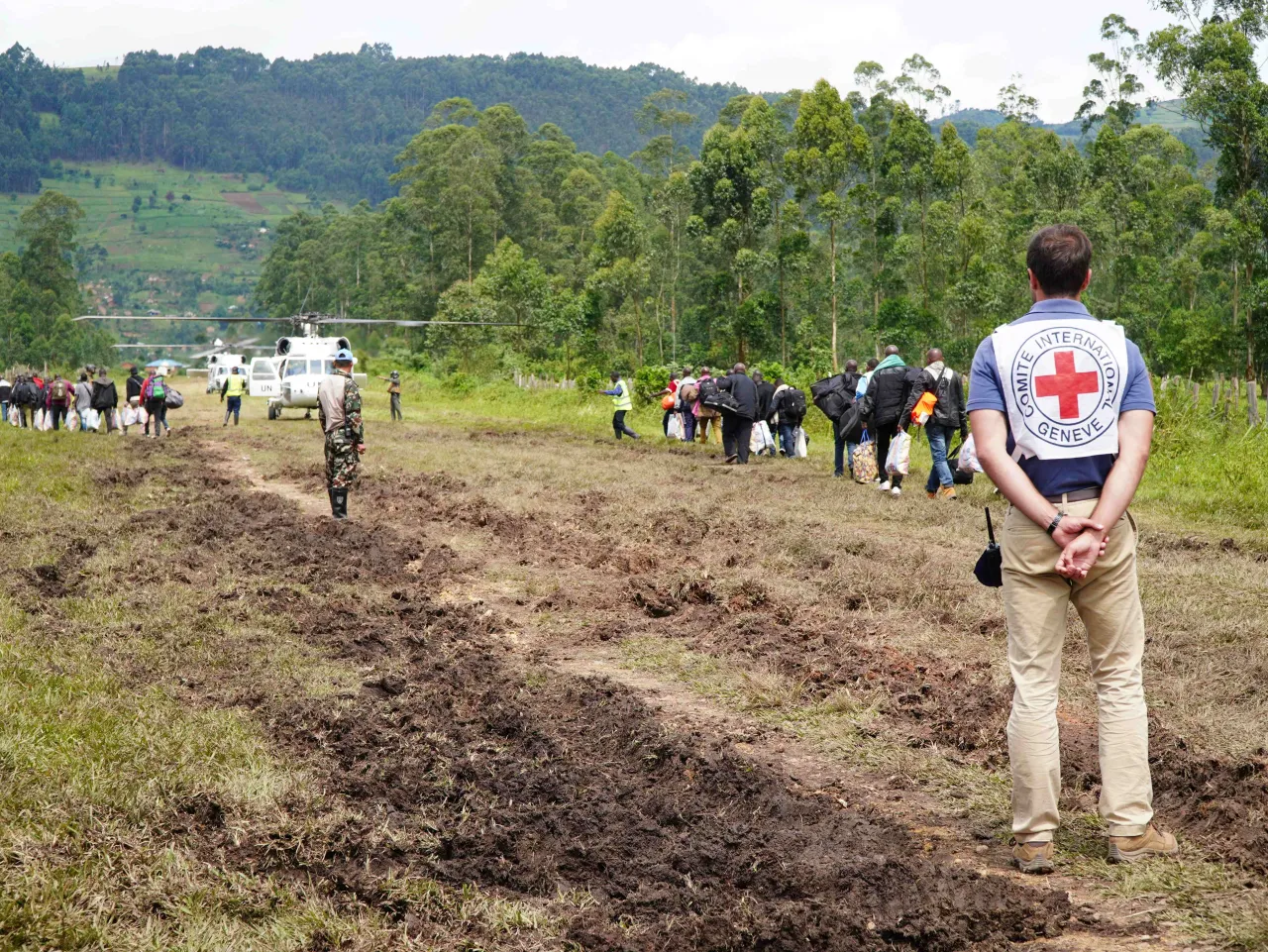 DRC operation  DRC operation ICRC staff member in the foreground on a dirt road, with people walking towards an aeroplane in the background