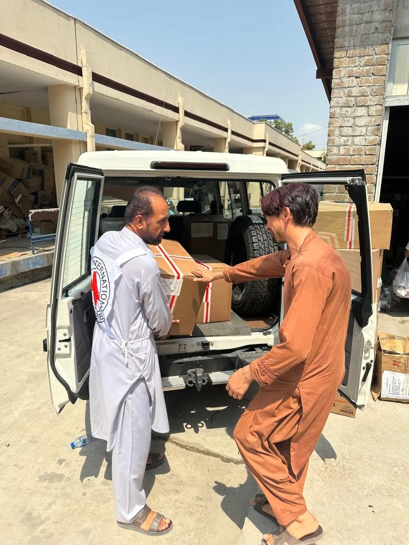 Afghanistan earthquake August 25 5 Credit Mohammad Masoud Samimi Two men load a box marked with a Red Crescent emblem into the back of a vehicle as part of relief efforts, with stacks of supplies visible in the background.