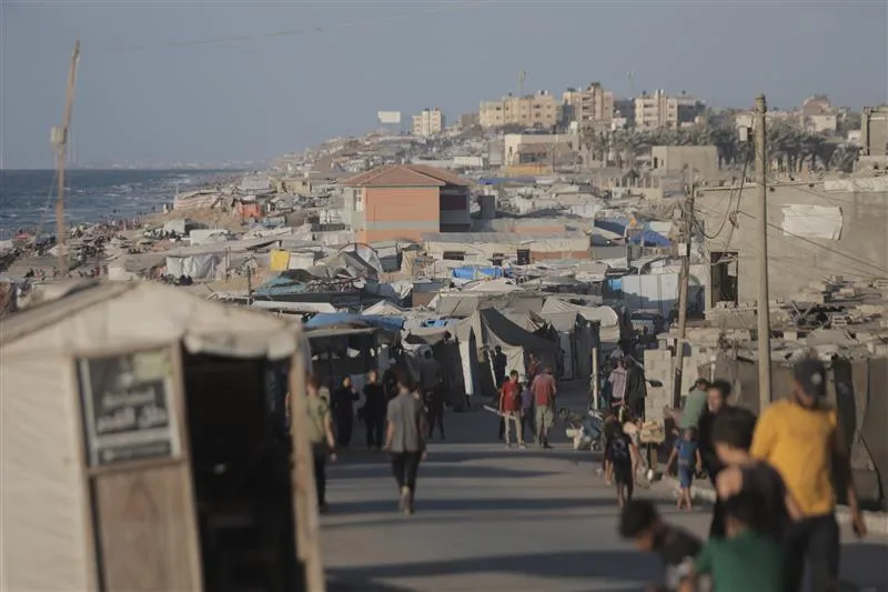 Gaza-City-September-2025-CREDIT-REUTERS-CONNECT_ANADOLU. Rows of makeshift tents and shelters crowd a coastal area, with people walking along a narrow road between them, and apartment buildings visible in the background.