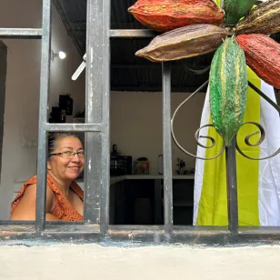Una mujer está sentada detrás de una ventana donde hay una escultura de una planta de cacao.
