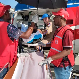 Two volunteers help a patient from a stretcher into an air ambulance