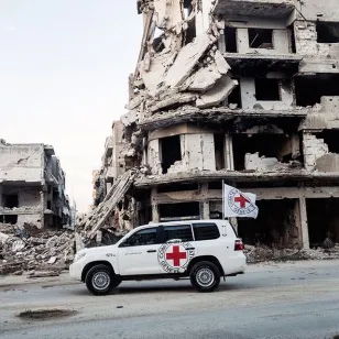 ICRC car next to buildings that have been destroyed by conflict 