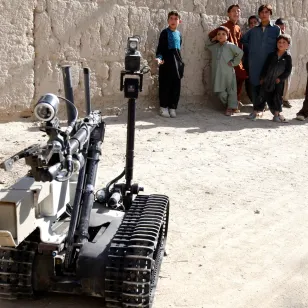 A robot used in war at the foreground while children look on in the background. 