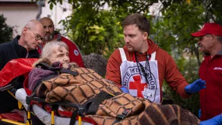 An ICRC medical staff member assists an elderly woman on a stretcher during an emergency situation.