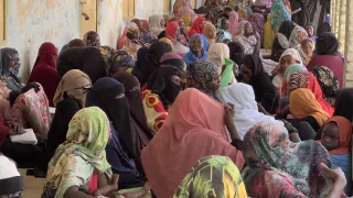 Sudanese women sitting by the wall of a school.