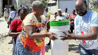 An ICRC staff helps a woman in Haiti to carry some buckets.