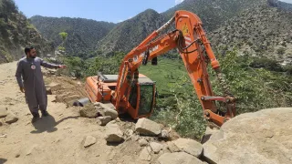 Afghanistan earthquake August 25 A man wearing a Red Crescent emblem points towards an excavator off a dirt road on a steep hillside in a mountainous area of Afghanistan, following the earthquake.
