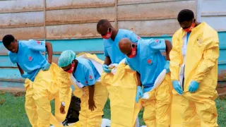 Red Cross volunteers in blue and yellow protective equipment prepare to carry out a safe and dignified burial during an Ebola outbreak in the Democratic Republic of the Congo