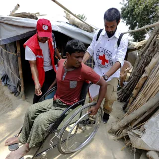 An ICRC field officer and a Bangladesh Red Crescent Society member are assisting a refugee from Myanmar with physical disabilities.