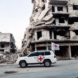 An ICRC vehicle next to buildings that have been destroyed by armed conflict. ICRC ICRC car next to buildings that have been destroyed by conflict