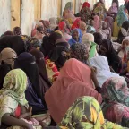 Sudanese women sitting by the wall of a school.