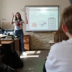 ICRC delelgate talking to students seated at desks in a classroom with information about explosive ordanances on a board behind her