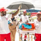 Ambulance workers shield a patient on a stretcher from the sun with an umbrella