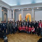 Policías, militares y otros funcionarios con miembros del Movimiento de la Cruz Roja posan para una foto grupal en un salón.