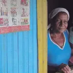 Una mujer con su hijo en brazo miran por la ventana de su hogar en Colombia.