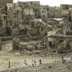 Group of children play football against a backdrop of destroyed houses.