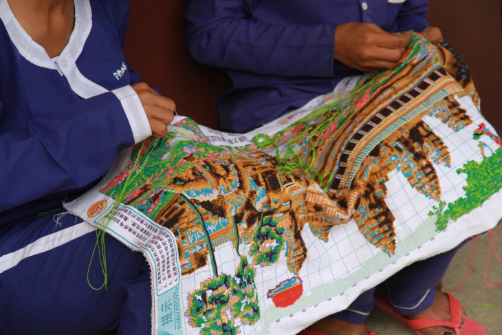 Female detainees embroider an image of Angkor Wat temple.